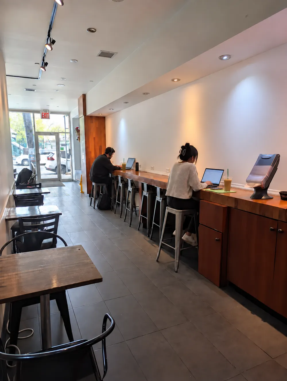 Two people working on laptops at the long wooden counter, iced drinks beside them